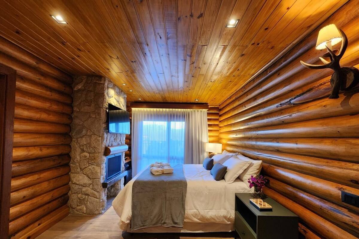 Une chambre dans une cabane en rondins, avec un mur en pierre, un lit avec des oreillers, une table de chevet et un téléviseur.