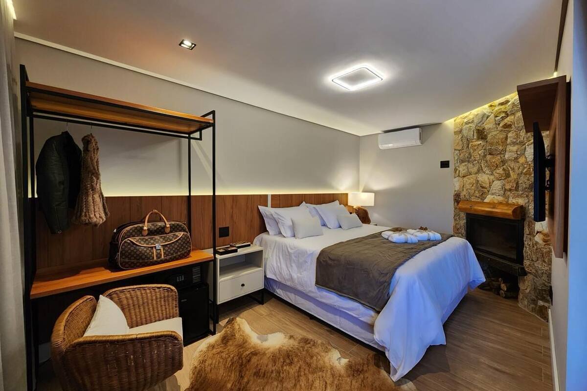 Une chambre moderne comprenant un lit, des tables de chevet, une armoire, un coin salon et un mur en pierre.