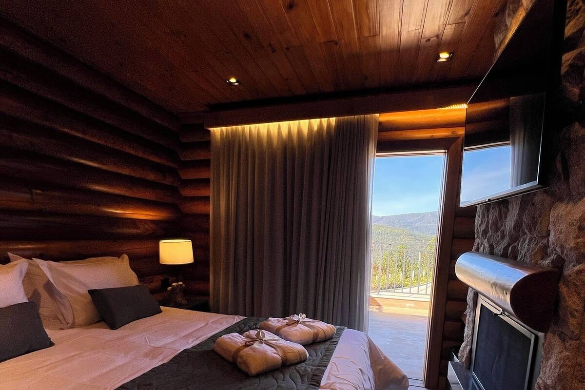 Une chambre située dans un chalet en rondins, avec un grand lit, une cheminée en pierre et une vue sur les montagnes.