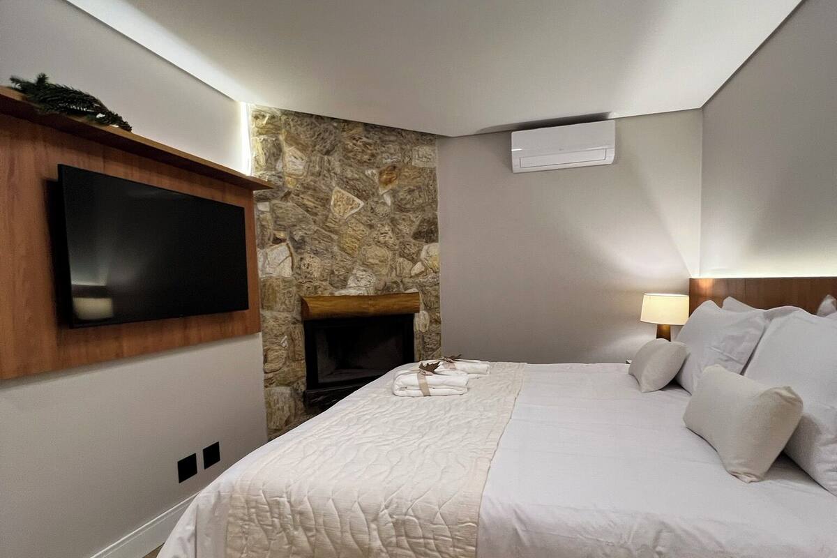 Une chambre avec un grand lit, un téléviseur fixé au mur, un mur en pierre et un luminaire au plafond.