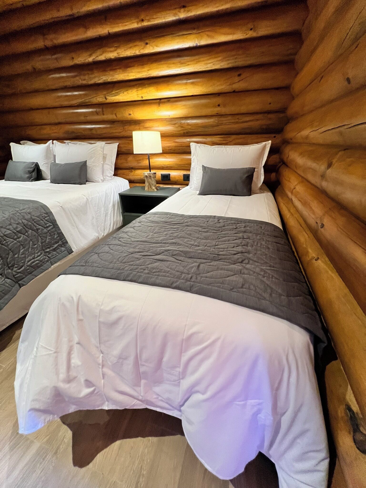 Ein Blockhausszimmer mit zwei Betten, jeweils mit einer grauen Steude und weißen Leinen.