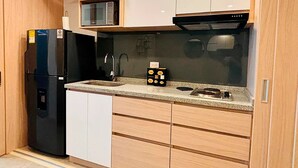 A compact kitchen with a black refrigerator, a microwave, and a stove. There are wooden cabinets and a countertop with a sink. - U-GO Belmonte Armenia (Armenia)
