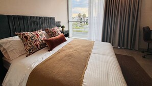 A hotel room with a large bed, a headboard, a view of the outdoors, and a window with curtains. - U-GO Belmonte Armenia (Armenia)