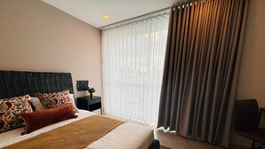 A hotel room with a large bed, a headboard, a nightstand with a lamp, a chair, and a window with curtains. - U-GO Belmonte Armenia (Armenia)