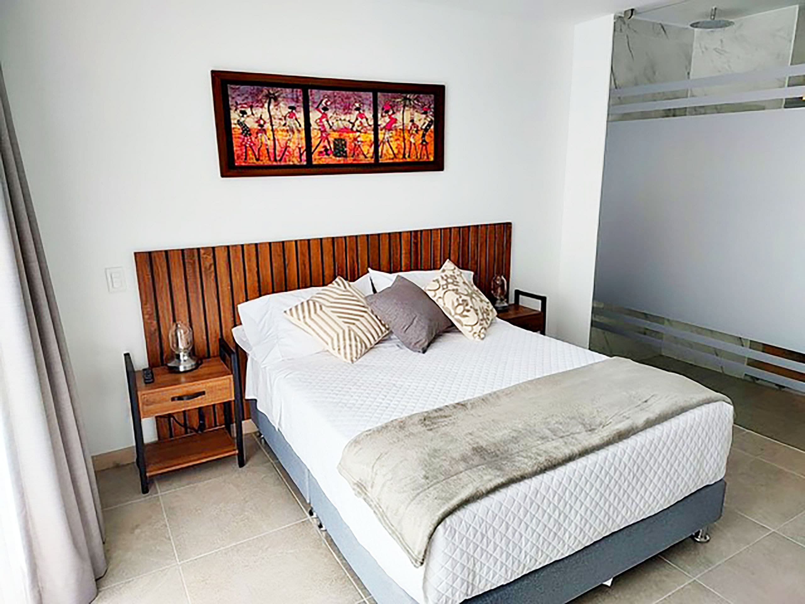 Een slaapkamer met een houten hoofdbord, een bed met witte lakens en een schilderij erboven.