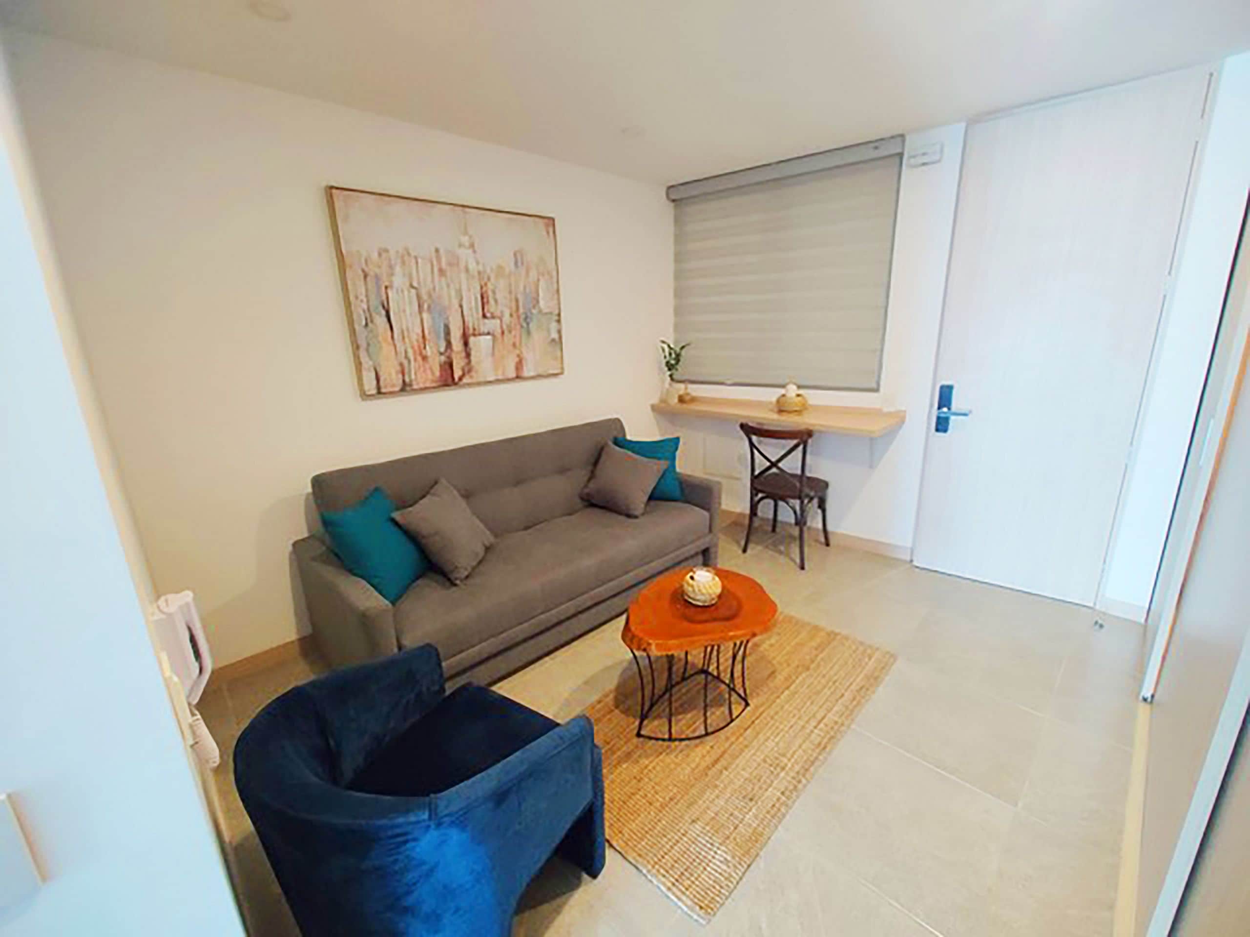 Een woonkamer met een bank, een fauteuil, een bijzettafeltje en een schilderij aan de muur.