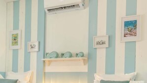 A hotel room with two beds, striped walls, a ceiling fan, an air conditioning unit, and a shelf with decorative items and a framed picture.