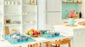A modern kitchen with white cabinetry, a white refrigerator, teal walls, and wooden chairs.