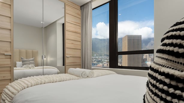 Ein modernes Hotelzimmer mit einem großen Bett, einer Glastrennwand und Blick auf eine Stadtlandschaft.