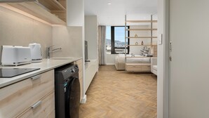 Eine moderne Küche mit Geschirrspüler, Kaffeemaschine und einer Arbeitsplatte mit einem Tablet. Ein Holzboden im Fischgrätmuster und ein Blick auf die Stadt durch große Fenster.
