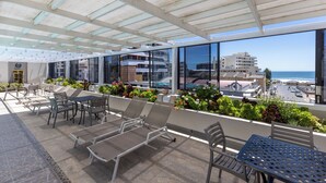 Una terrazza sul tetto con lettini e tavoli, vista sulla città e sull'oceano.