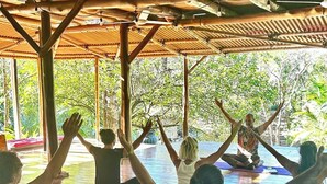 Un grupo de personas sentadas sobre esterillas de yoga en una habitación con suelo de madera y techo de bambú.