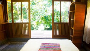Una habitación con una cama, vistas a la vegetación a través de puertas abiertas y estanterías de madera.