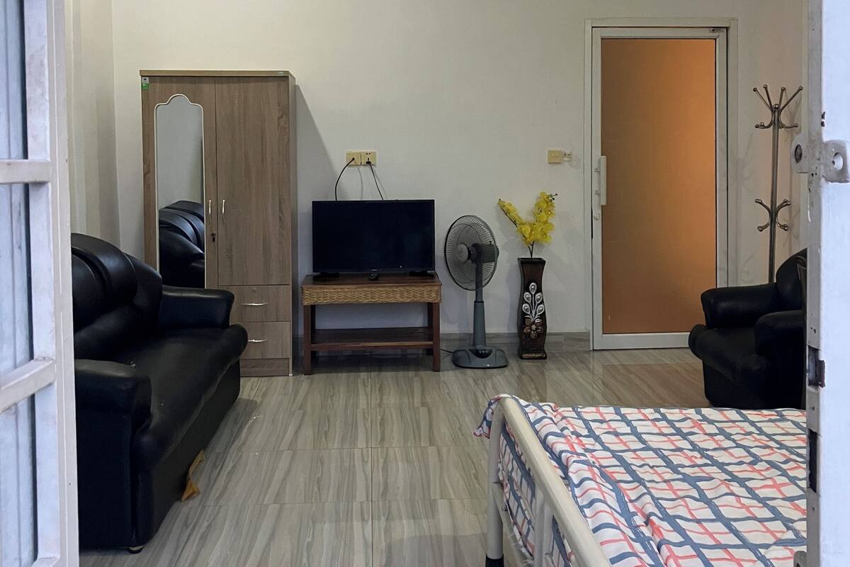 Una habitación amplia con una cama, un sofá, un televisor en un mueble, un ventilador y una puerta.