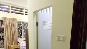 A room with a bed, a small wooden table, a blue rug, a wicker chair, and a door with a window. - Cannarata (Phnom Penh)