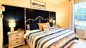 A bedroom with a bed, nightstands, a headboard, a window, and a ceiling fan. - Experience the Wild Beauty of Sunset Village from Your Private Balcony (Sunset Beach)
