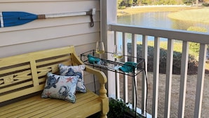 A porch with a bench, a sign reading "BEACH HOUSE", and a view of a lake. - Experience the Wild Beauty of Sunset Village from Your Private Balcony (Sunset Beach)