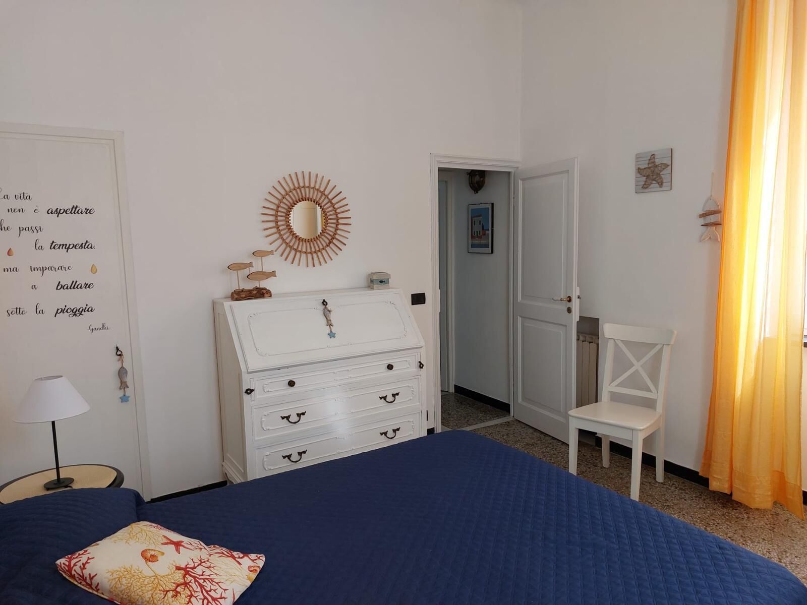 Une chambre à coucher comprenant un lit, une commode, une chaise et un mur orné d’un miroir décoratif et d’une citation.