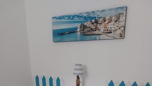 A bedroom with two beds, a nightstand, a lamp, and a painting of a coastal town. - Casa Annalù With Garden Wifi Bogliasco (Bogliasco)