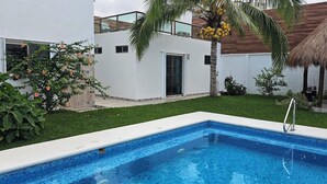 A swimming pool with a clear blue water, surrounded by a well-maintained lawn and a white building with a balcony. - Palancar house with beautiful swimming pool and private palapa (San Miguel de Cozumel)