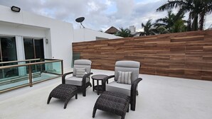 A modern outdoor seating area with wicker furniture, a glass balustrade, and a wooden wall. - Palancar house with beautiful swimming pool and private palapa (San Miguel de Cozumel)