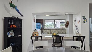 A modern kitchen with a large window, a dining area with two chairs, and a black entertainment unit with various items. - Palancar house with beautiful swimming pool and private palapa (San Miguel de Cozumel)