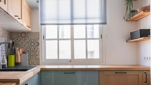 A modern kitchen with light wood cabinets, a grey countertop, and a window with blinds.