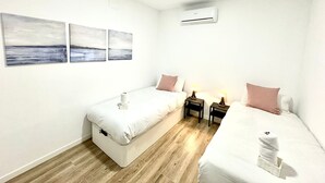 Ein Hotelzimmer mit zwei Betten, Holzboden, Wandklimaanlage und drei Bildern.