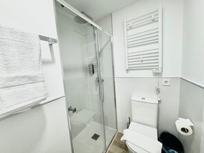 A modern bathroom with a glass-enclosed shower, a toilet, and a towel rack.