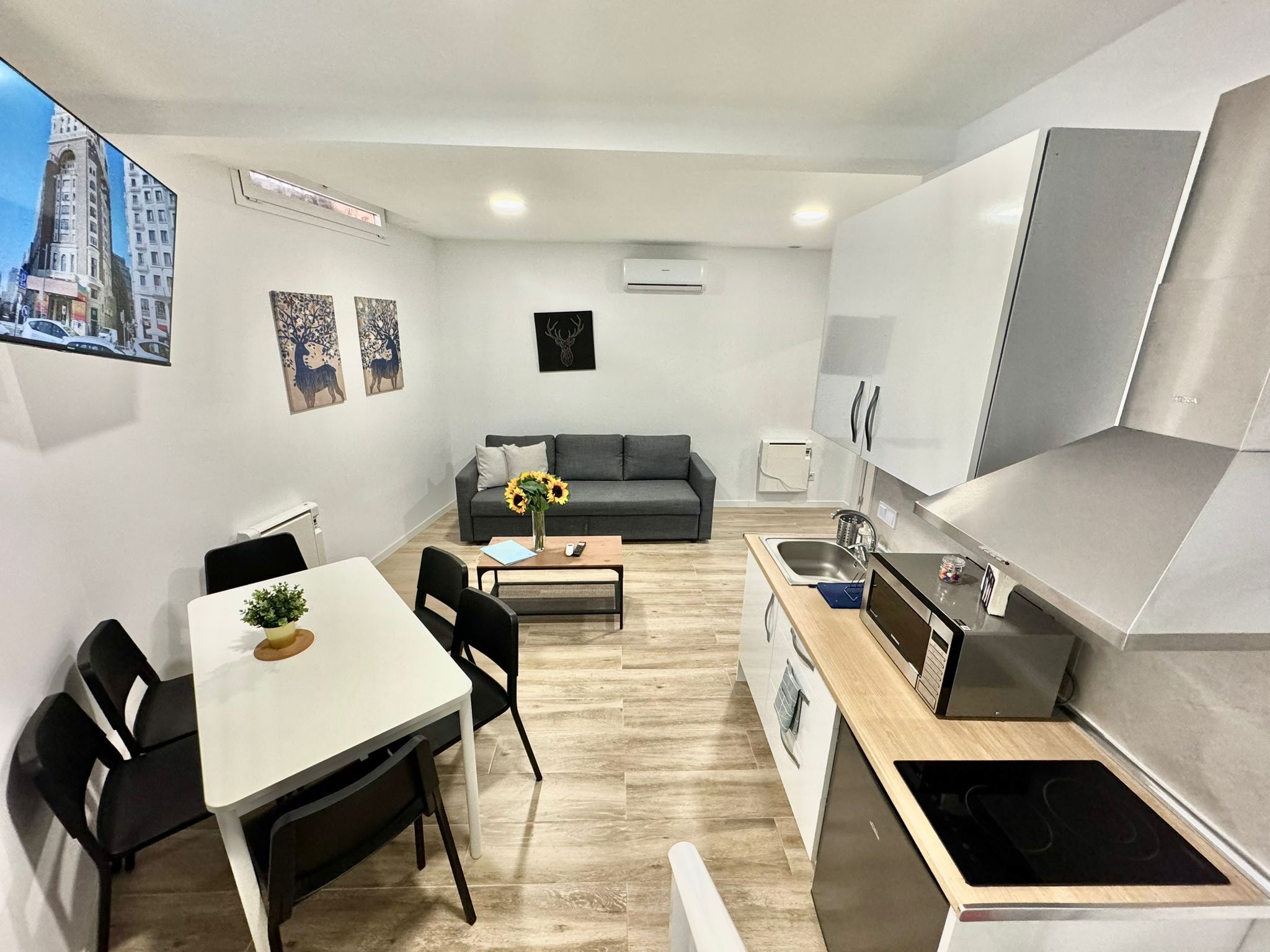 Ein kompakter Wohnbereich mit Essbereich, Sofa, Küchenzeile und einem an der Wand befestigten Fernseher.