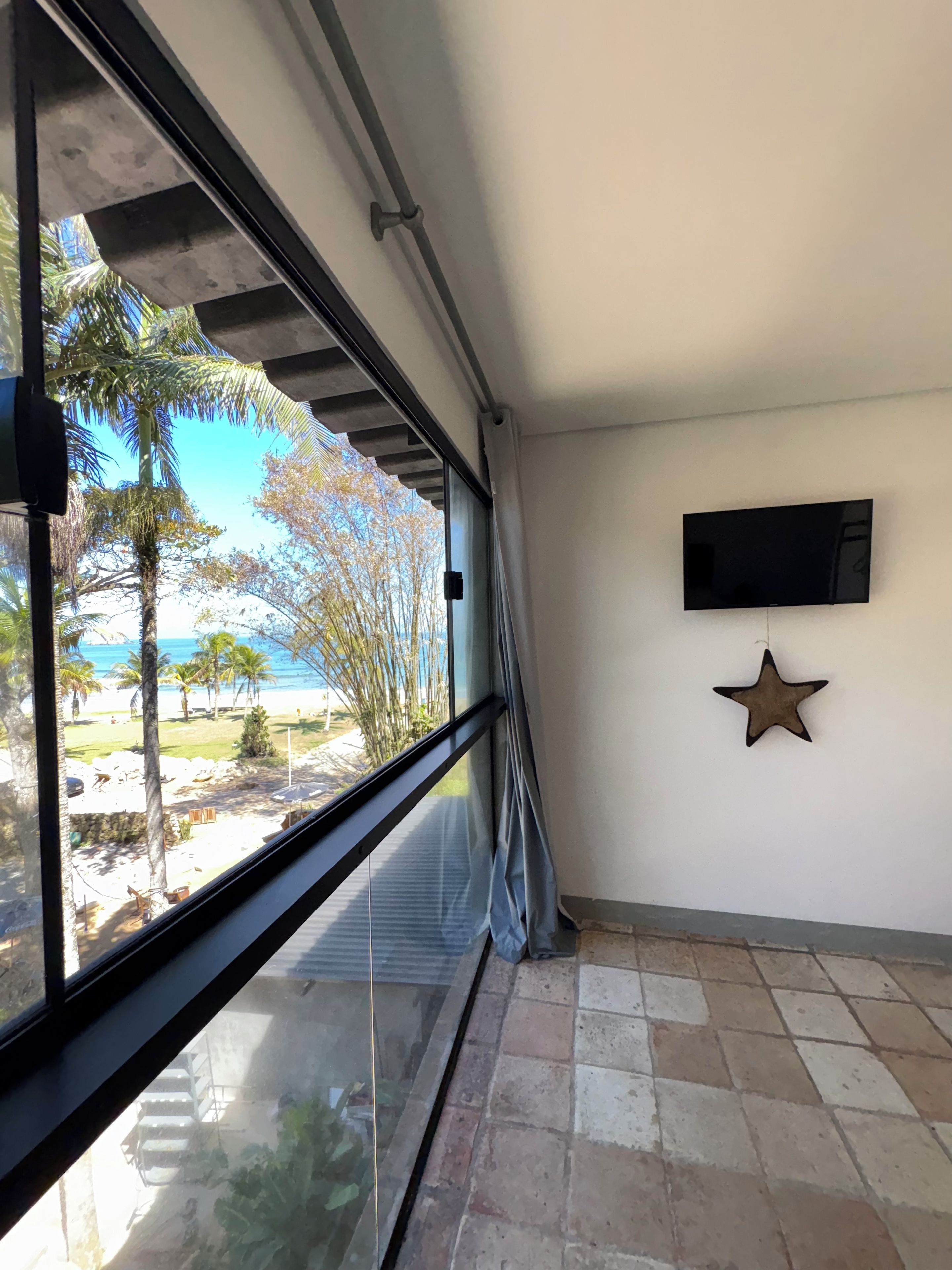 Een kamer met een groot raam met uitzicht op een strand, een wandtelevisie en een ster decoratie.