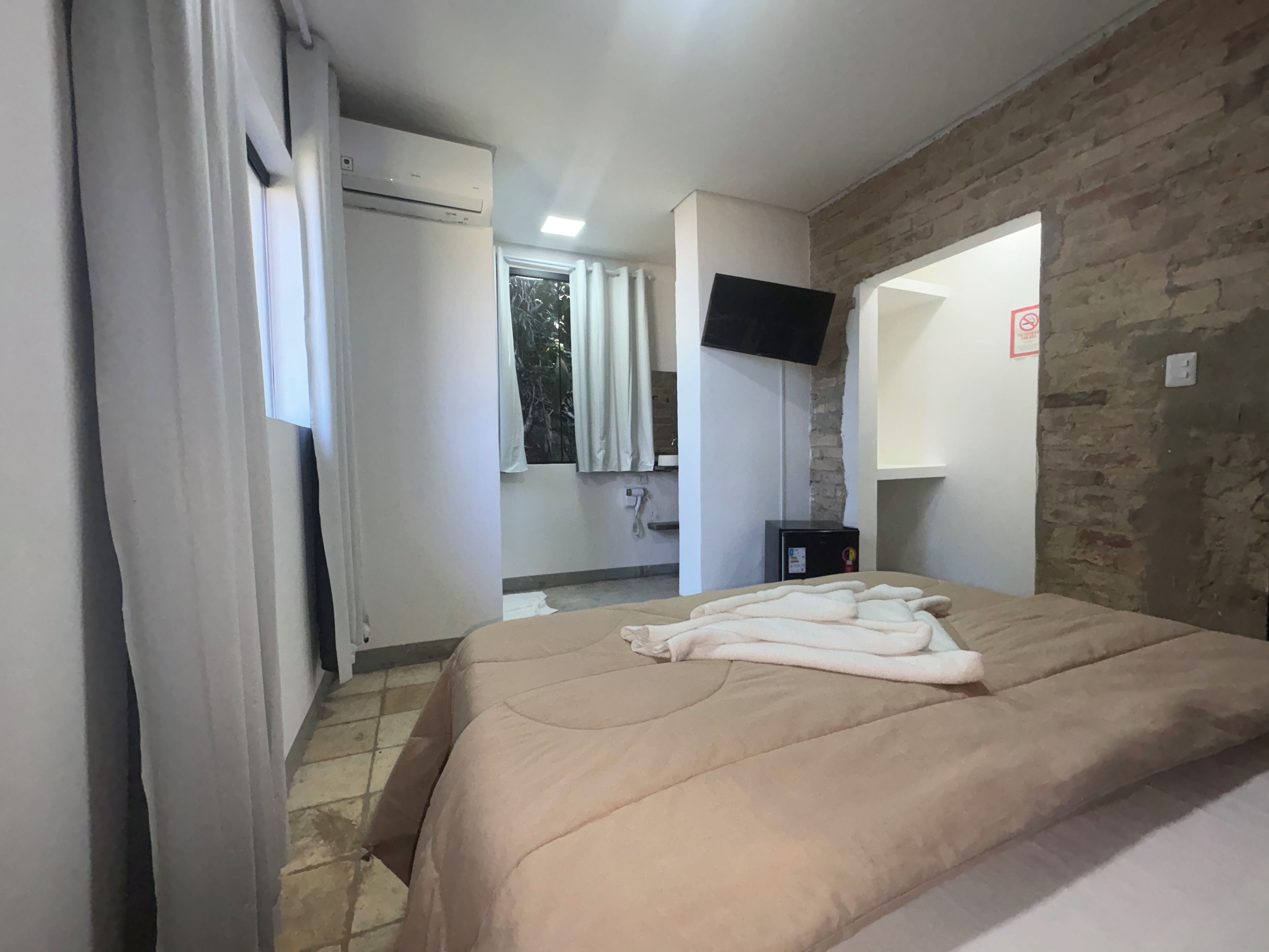 Habitación de hotel con cama, televisión, un escritorio pequeño y una pared de ladrillo.