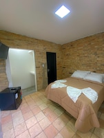 Un dormitorio con pared de ladrillo, una cama con ropa blanca, una maleta negra y una puerta.