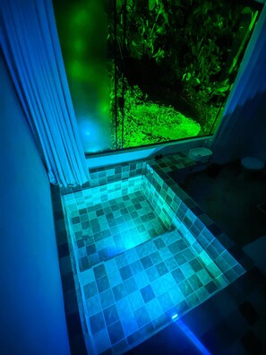 A corner of a room with a tiled floor and a view of a garden through a window.