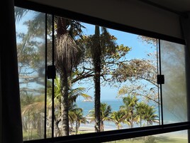 Une vue à travers une fenêtre donnant sur une plage et des palmiers.