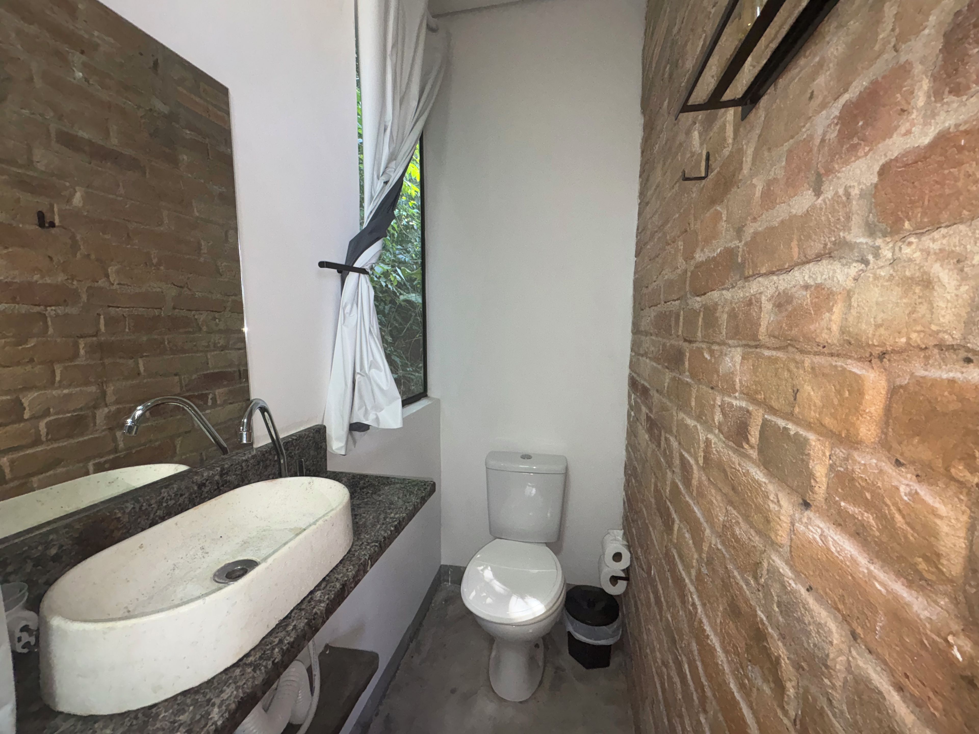 Un baño con lavamanos de encimera de granito, inodoro blanco y cubo de basura negro.