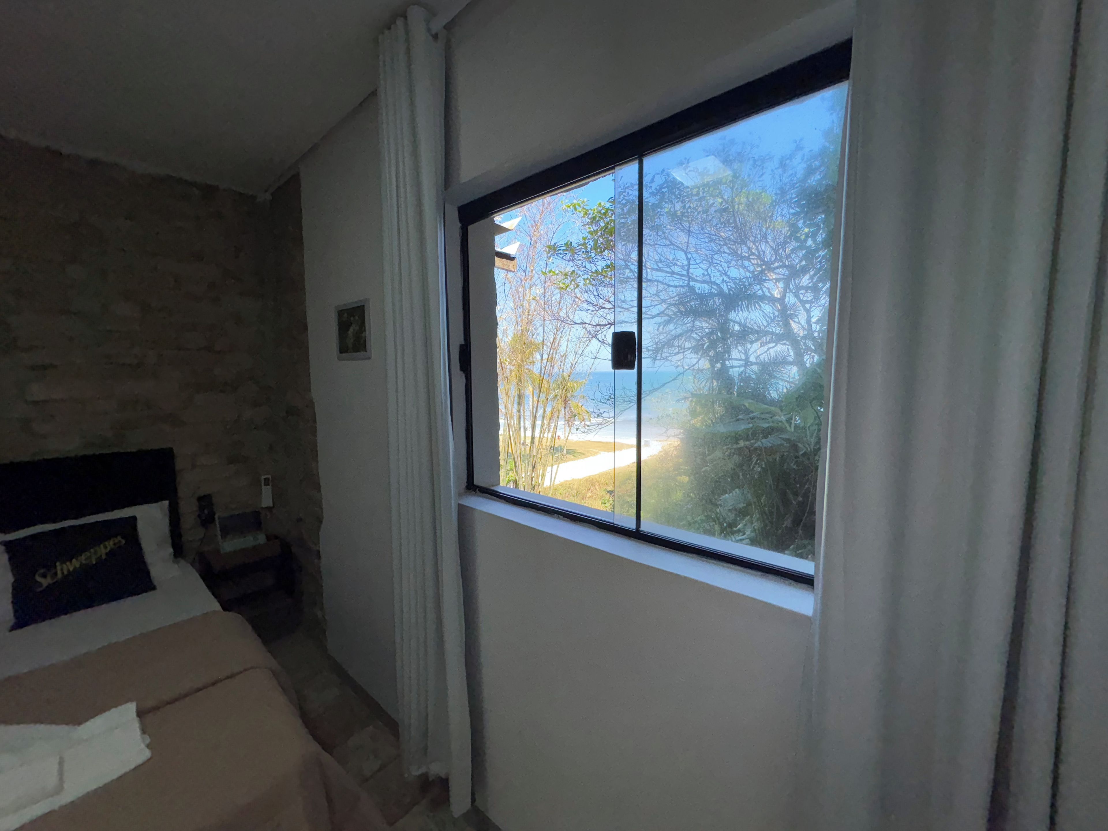 A bedroom with a large window, a bed with a headboard, and a stone wall.