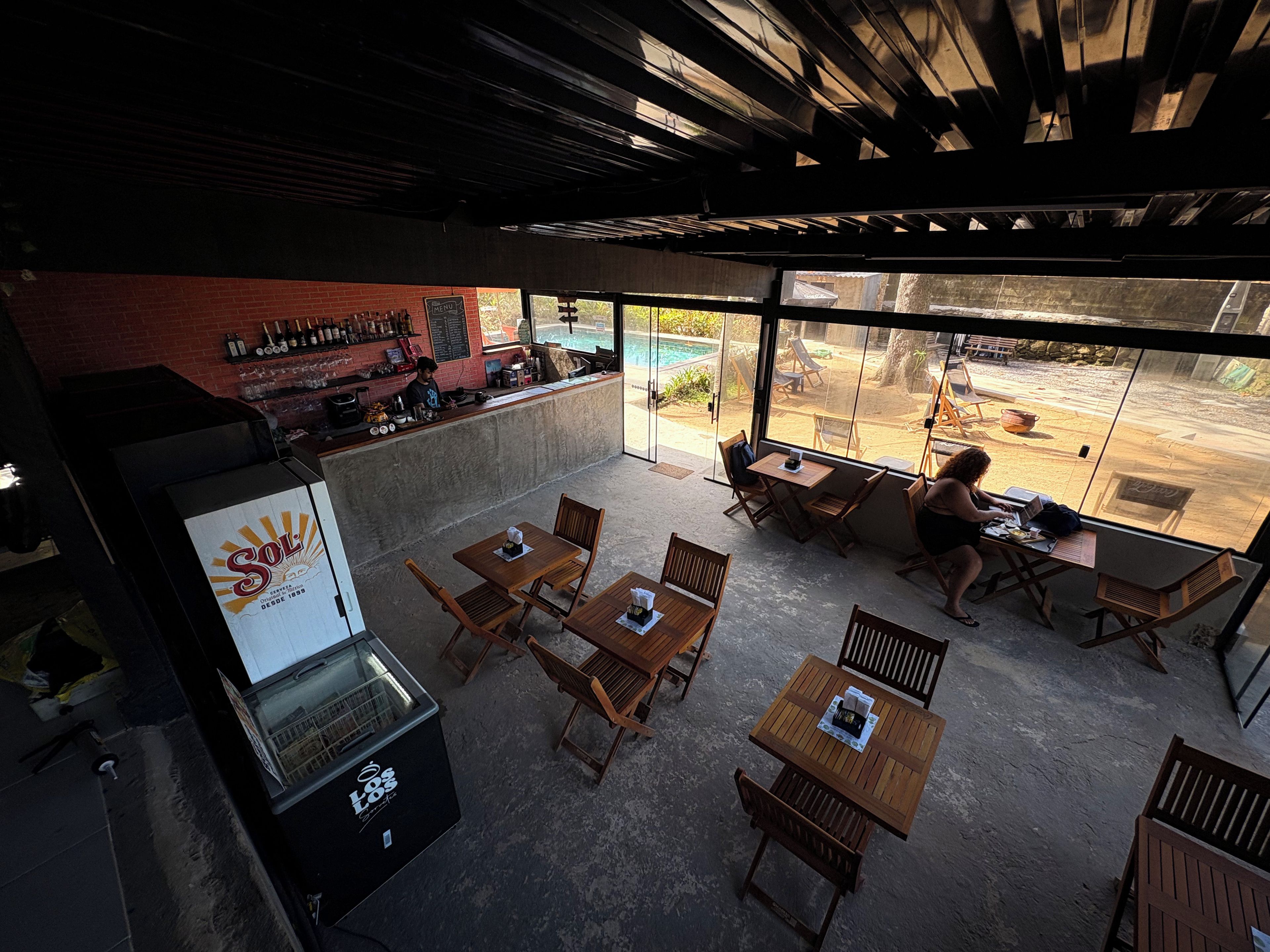 An outdoor seating area with tables and chairs, a bar with bottles, and a view of a swimming pool.