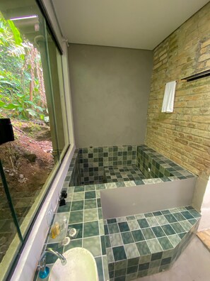 A bathroom with a bathtub, a sink, and a window overlooking greenery. - Raízes do Mar (Guarujá)