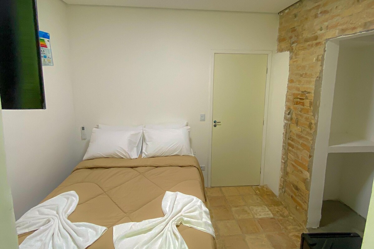 A small, clean room with a bed, a door, and a brick wall.