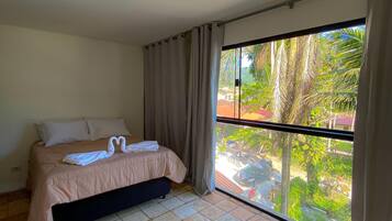 Un dormitorio con cama, ventana con cortinas y piso de baldosas.