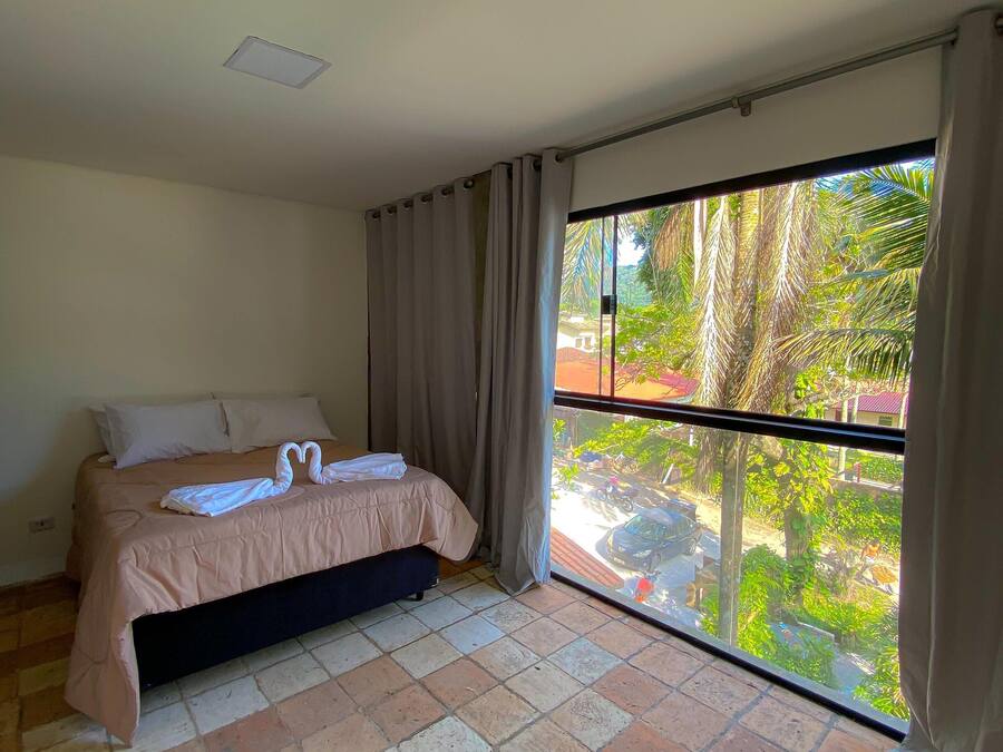 Un dormitorio con cama, ventana con cortinas y piso de baldosas.