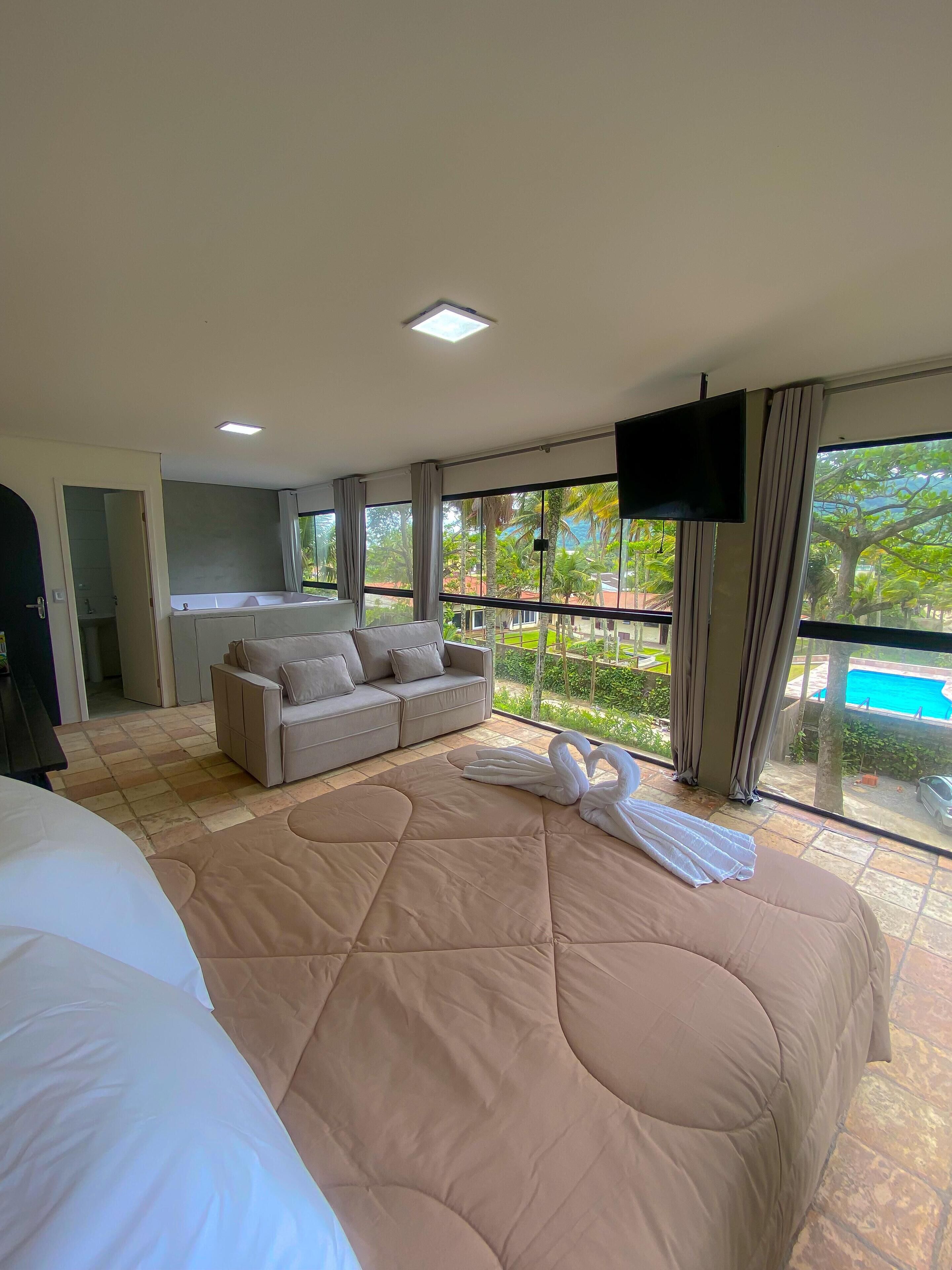 Habitación de hotel con una cama grande, un sofá, un televisor y un balcón con vista a la piscina.