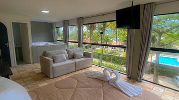 Habitación de hotel con una cama grande, un sofá, un televisor y un balcón con vista a la piscina.