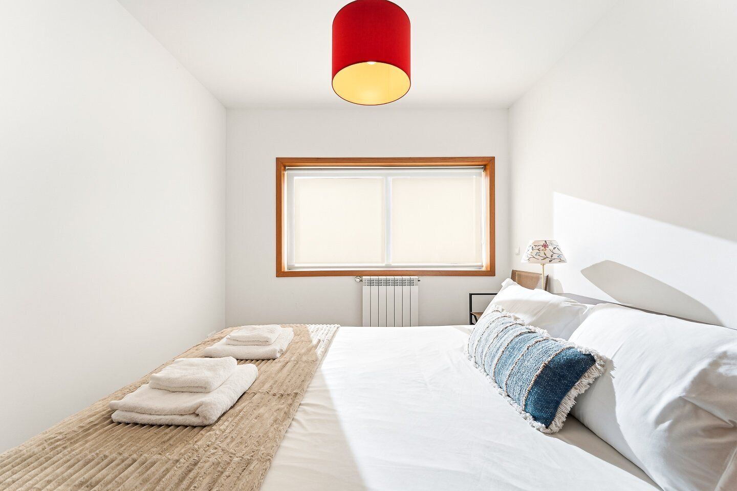 Une chambre à coucher avec un lit, une fenêtre, un radiateur et une lampe suspendue rouge.