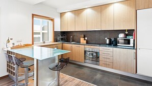 A modern kitchen with wooden cabinets, a glass island, stainless steel appliances, and a window. - GuestReady - Seaside Experience in Moledo (Moledo)