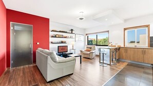 A modern living room with a sofa, a TV, and a bookshelf. There's a kitchen area with a bar and a window. - GuestReady - Seaside Experience in Moledo (Moledo)