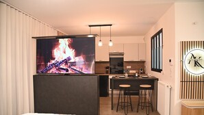 Een moderne hotelkamer met een grote tv waarop een haard te zien is, een kitchenette en een eethoek met krukken.