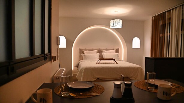 Hotelkamer met een bed centraal onder een ronde lamp, nachtkastjes met lampen en uitzicht buiten door een raam.