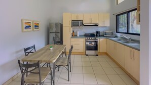 A compact kitchen with a dining table, chairs, a refrigerator, microwave, stove, and a window with a view.